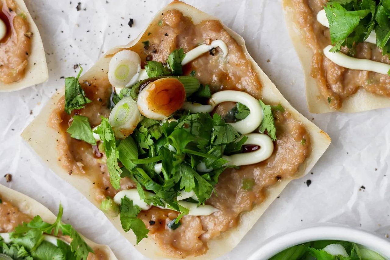 Wontons crocantes de frango ao forno ao lado de molho barbecue japonês, folhas verdes e um copo de água mineral