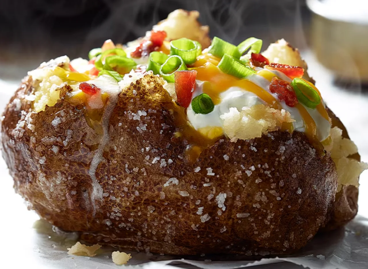 Batata assada aberta, recheada com peito de frango grelhado, quinoa, abacate e folhas verdes ao lado de halteres