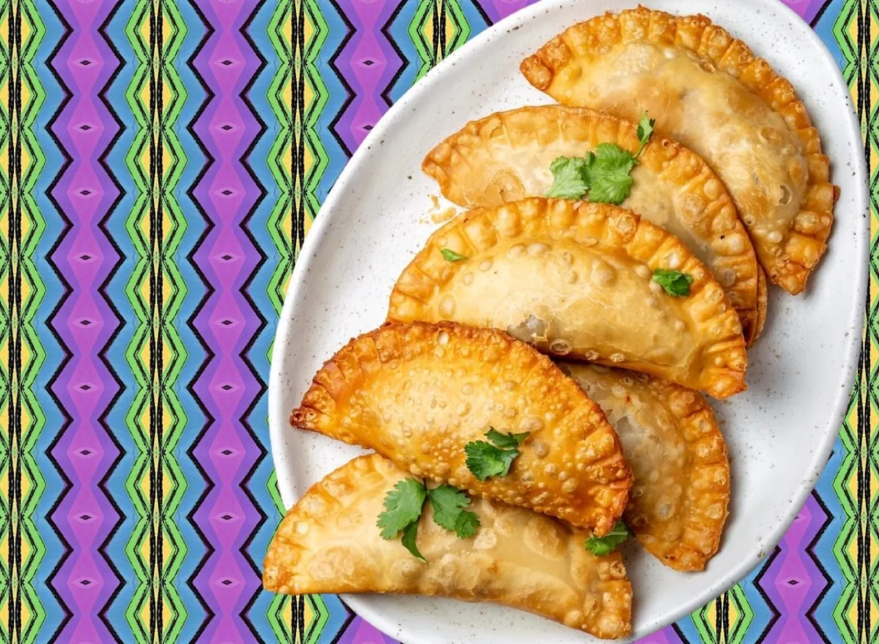 Empanada de carne dourada ao lado de salada verde, tomate cereja e suco natural em copo de vidro