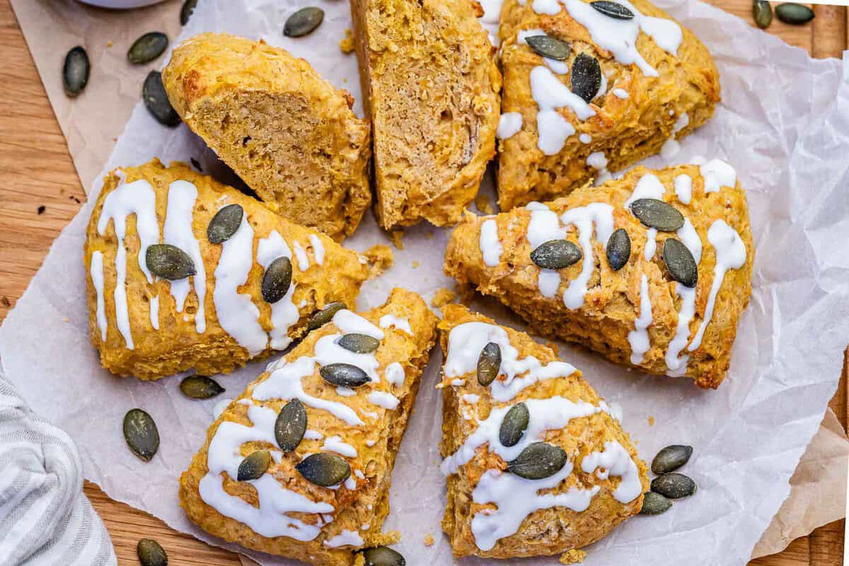 Scones de abóbora dourados em uma assadeira, ao lado de purê de abóbora e uma tigela de farinha