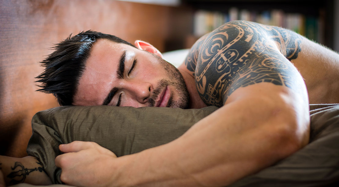 Atleta musculoso dormindo com máscara de CPAP ao lado de halteres e suplementos em um quarto escuro