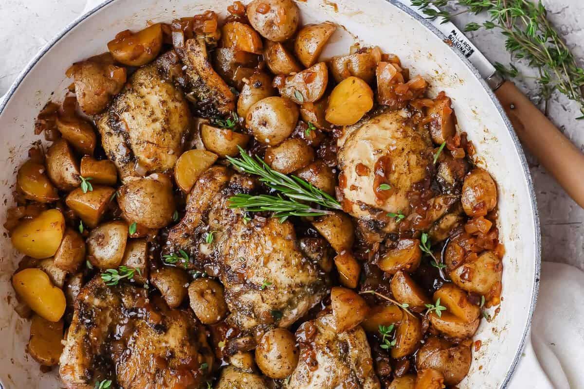 Coxas de frango douradas em panela, ao lado de cidra de maçã, cebola e alho, com colher de manteiga derretida