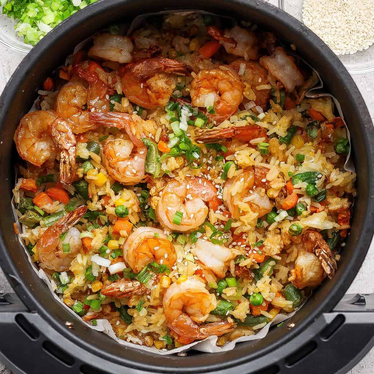 Bowl de arroz frito dourado com vegetais e ovo, servido ao lado de uma air fryer aberta sobre uma bancada moderna