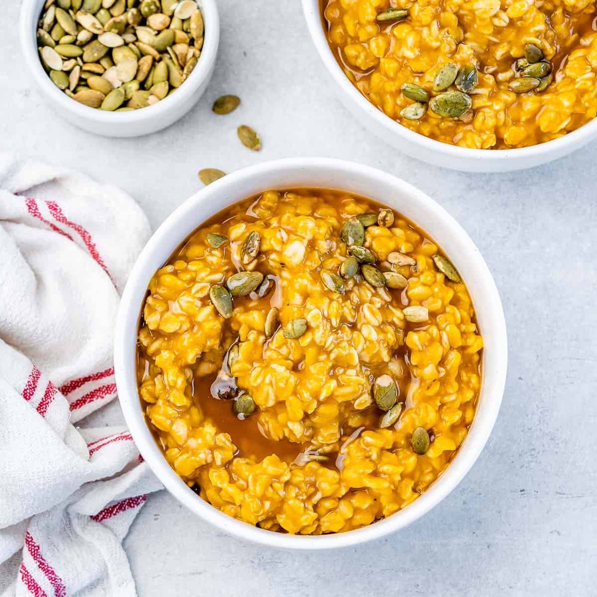 Tigela de oatmeal cremosa com purê de abóbora, canela polvilhada, nozes picadas e colher de madeira ao lado