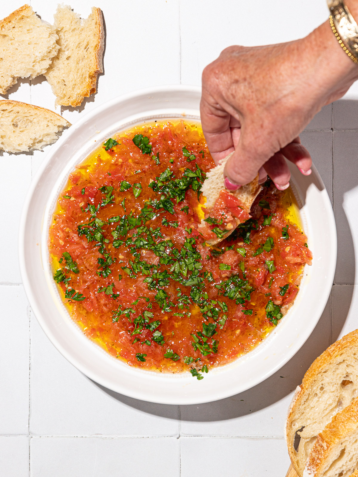 Garfo mergulhando em um dip cremoso de tomate e alho, ao lado de uma garrafa de azeite extra virgem e ramos de alecrim