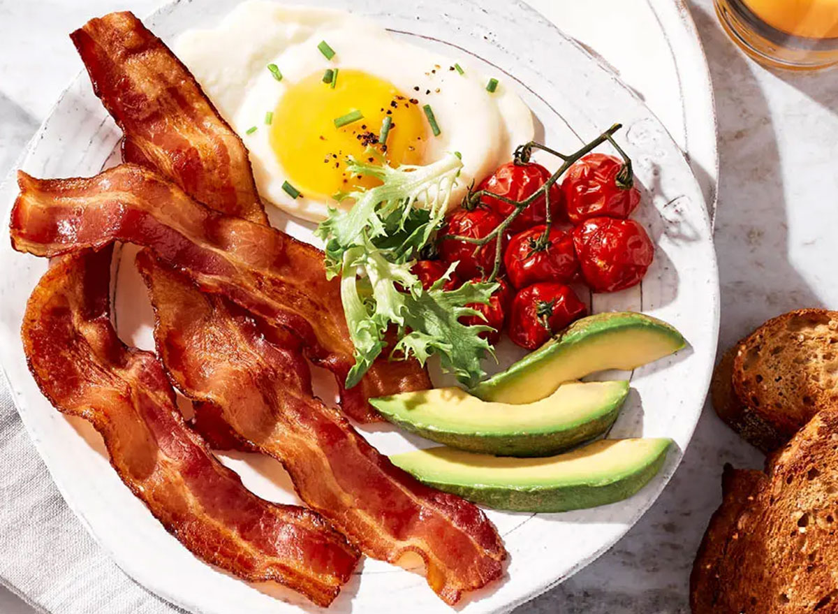 Fatias de bacon crocante ao lado de ovos frescos e vegetais verdes em uma mesa de café da manhã equilibrada