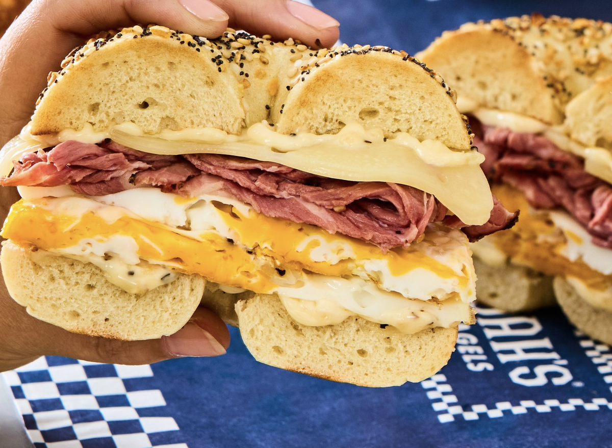Bagel dourado com cream cheese e sementes sobre uma mesa de madeira ao lado de uma xícara de café e frutas frescas