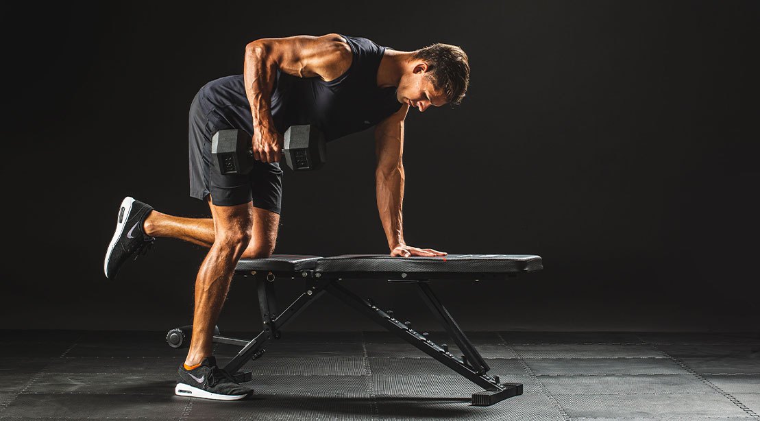 Uma pessoa realizando um bent-over row com um barbell pesado, com o peso do braço direito mais alto do que o esquerdo, indicando uma postura inadequada