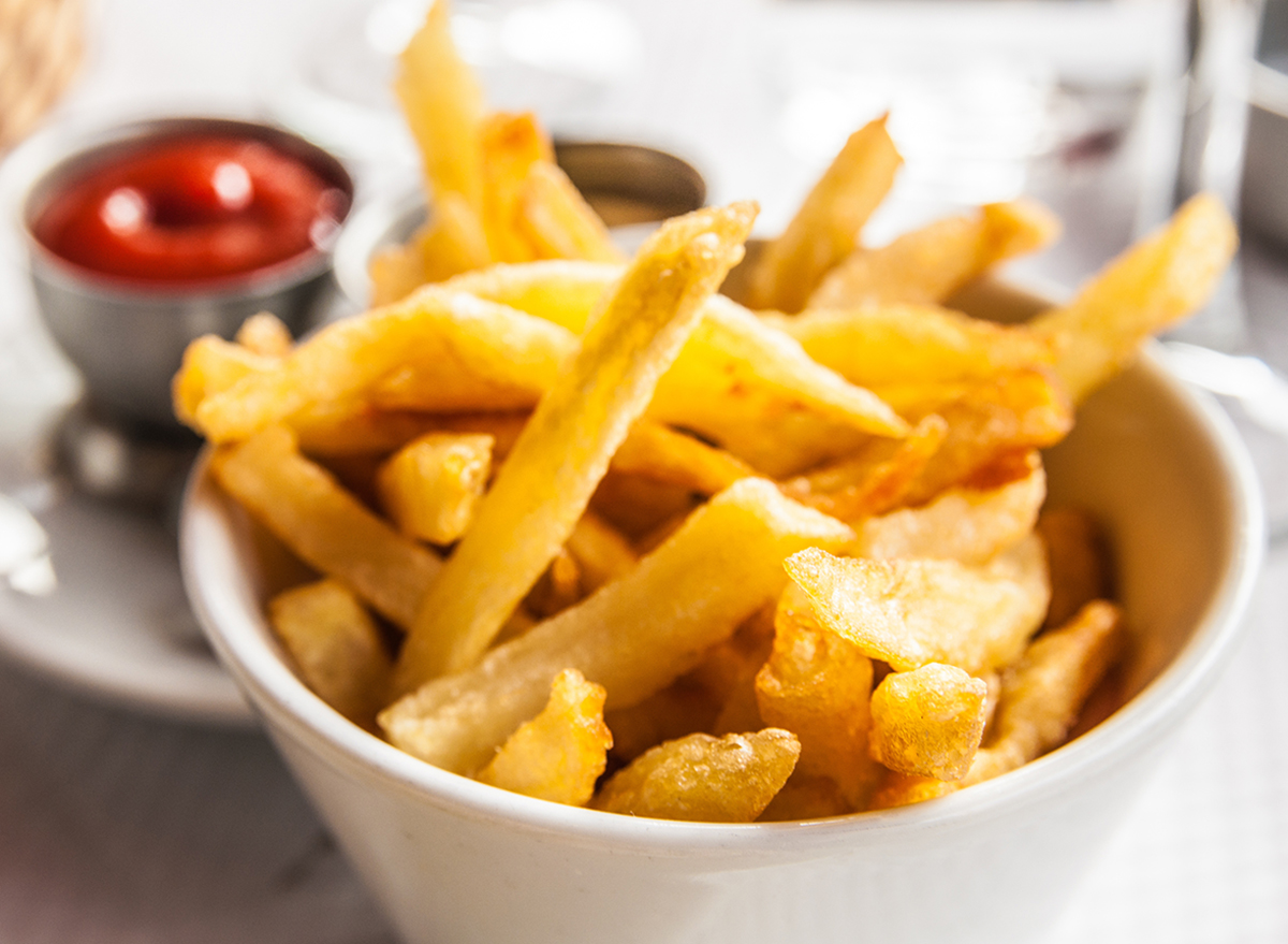 Porção de batatas fritas douradas e crocantes dispostas em uma tigela ao lado de um pacote aberto no freezer