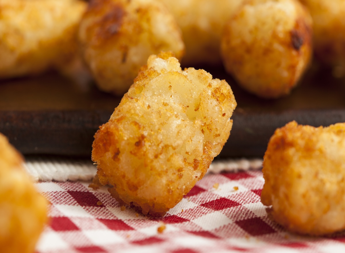 Uma mulher cozinhando batatas congeladas no micro-ondas com uma colher de pau ao lado