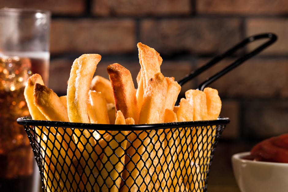 Porção de batatas fritas congeladas ao lado de uma balança de cozinha sobre uma mesa de madeira clara