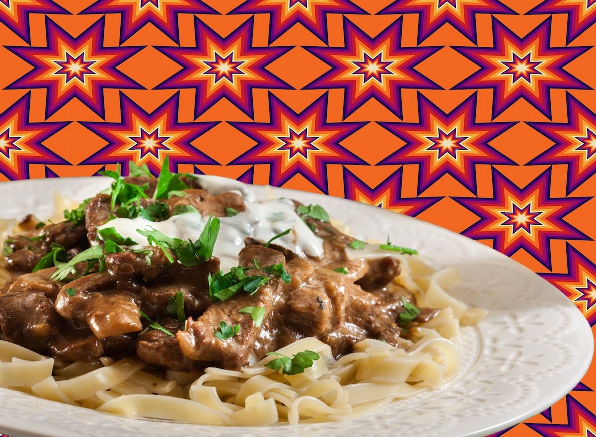 Corte magro de carne bovina ao lado de legumes frescos e uma tigela de molho cremoso, tudo sobre uma tábua de madeira