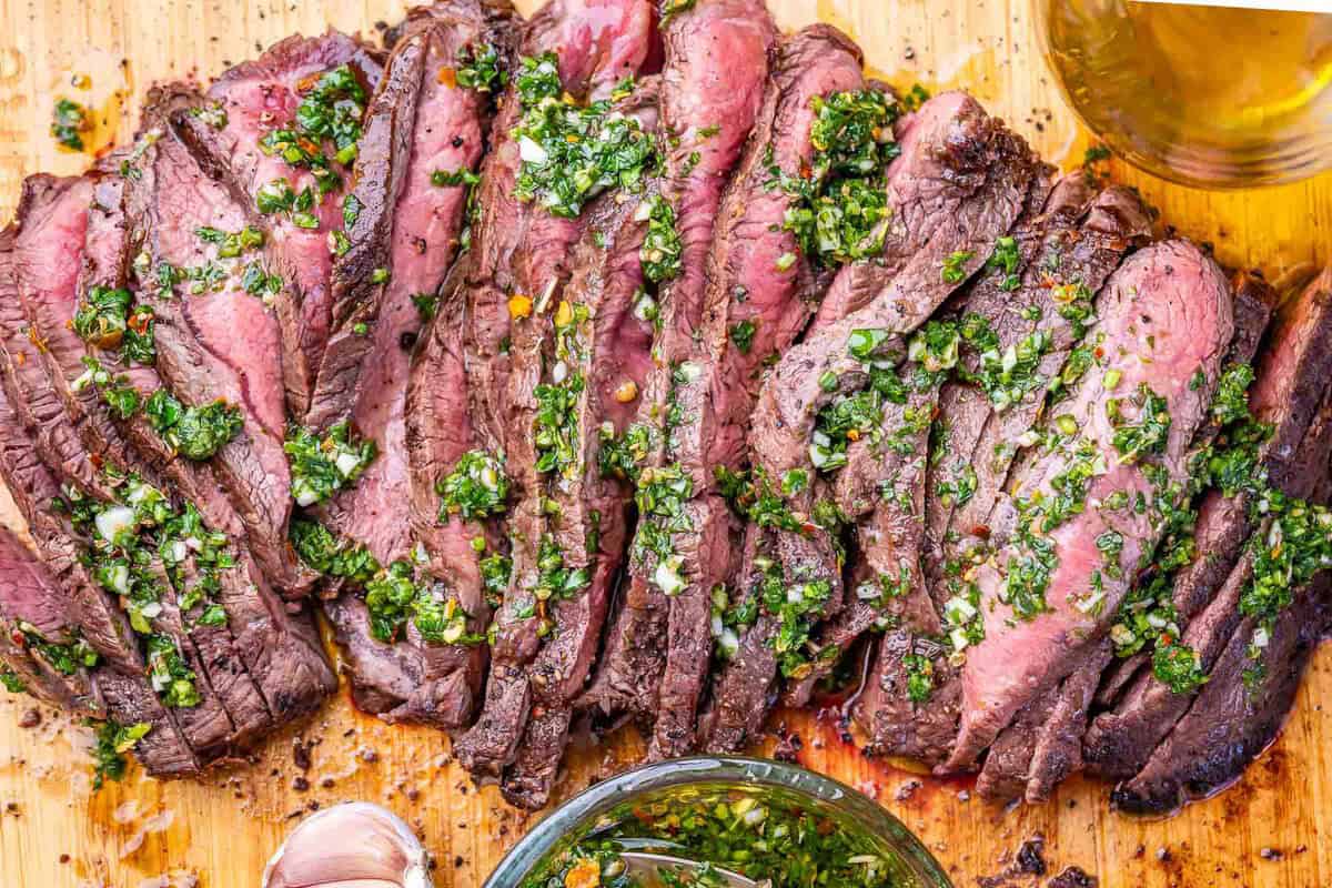 Bife grelhado suculento coberto com molho chimichurri fresco sobre uma tábua de madeira ao lado de ervas aromáticas