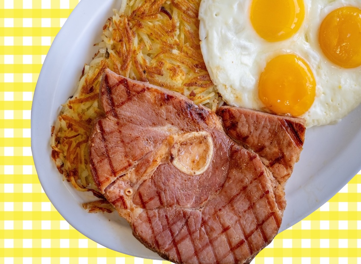 Bife de presunto suíno grelhado e suculento em um prato, acompanhado de vegetais frescos e talheres sobre uma mesa