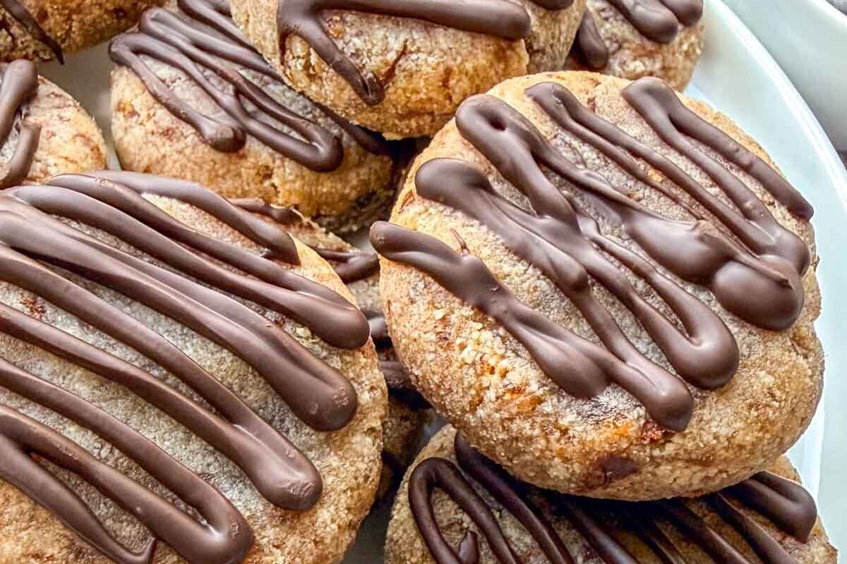 Biscoitos de tâmara e amêndoas dispostos sobre uma mesa de madeira ao lado de tâmaras frescas e uma xícara de café