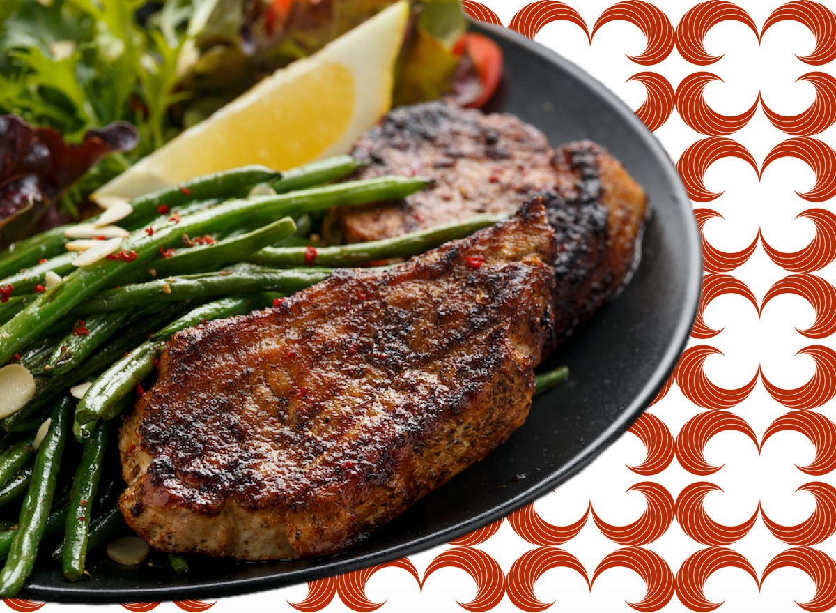 Bisteca de porco grelhada ao lado de salada verde, legumes assados e um copo de água