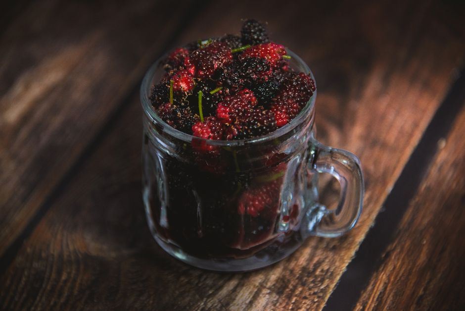 Uma pessoa segurando uma xícara de suco de blueberry, com uma pilha de frutas vermelhas ao fundo