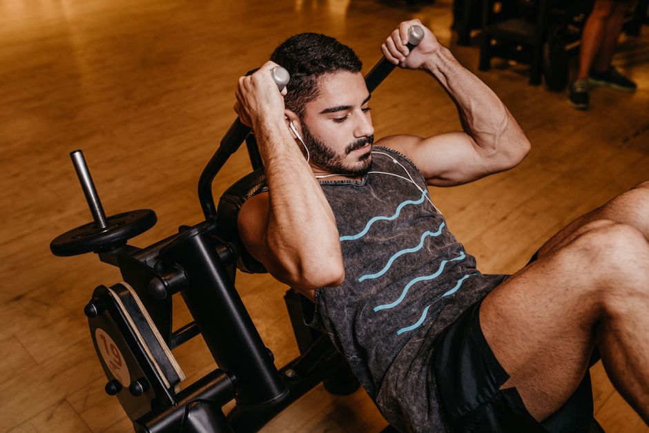 Peso livre em mãos, barra de peso sobre os ombros, com um modelo masculino em pose de flexão