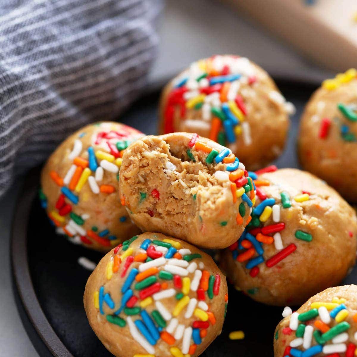 Bolas de proteína de cashew butter e aveia sobre uma tábua, ao lado de um pote de proteína em pó e um bolo de aniversário decorado