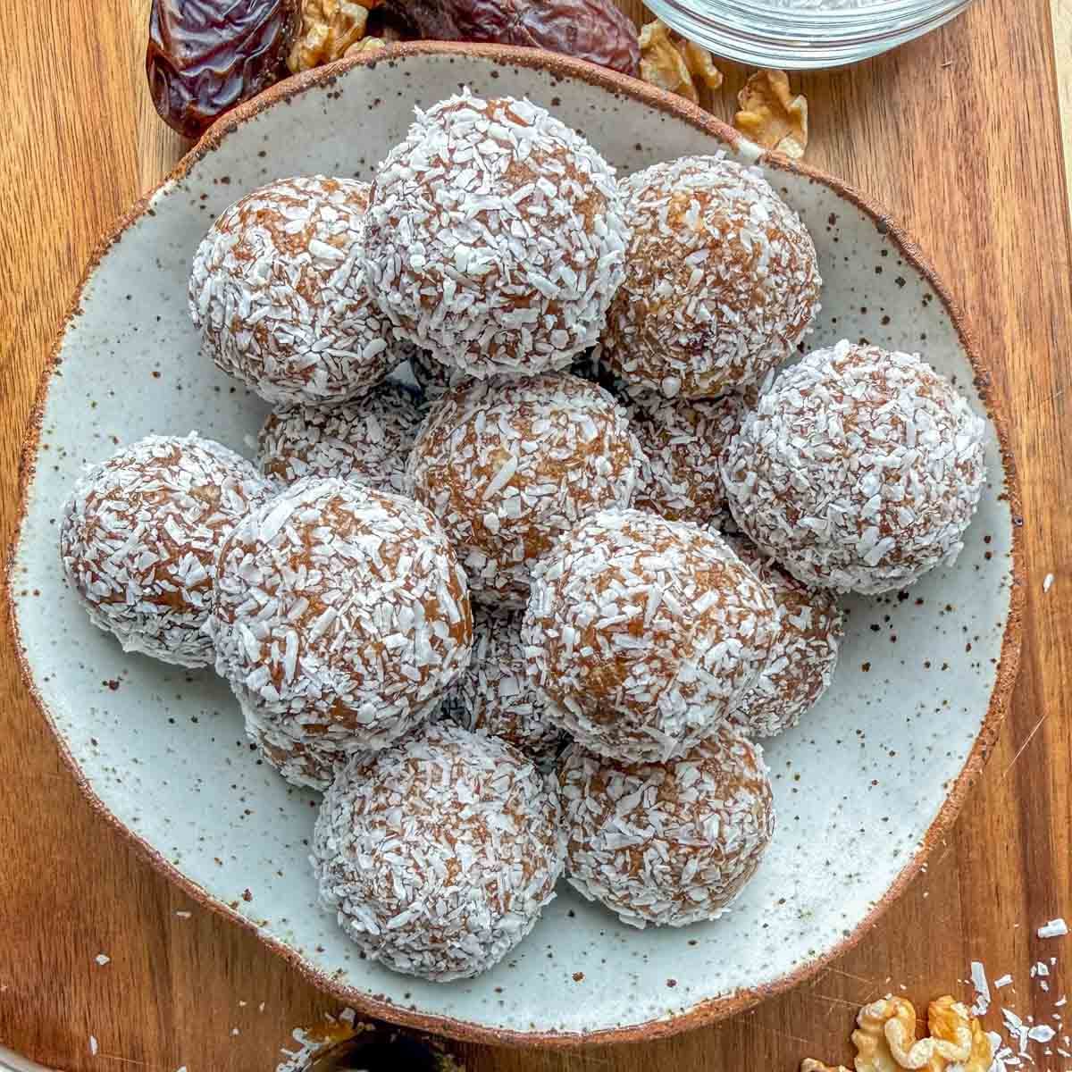 Bolinhas de tâmara e nozes dispostas em uma tigela rústica ao lado de tâmaras inteiras e nozes sobre uma mesa de madeira