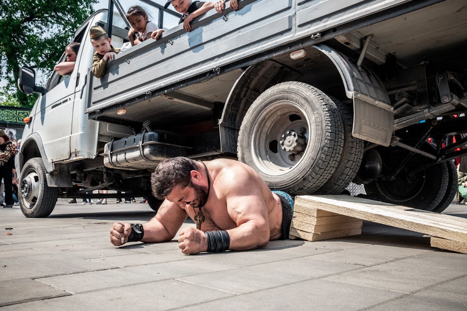 Brian Shaw posa imponente ao lado de troféus gigantes e equipamentos de strongman em um ginásio profissional
