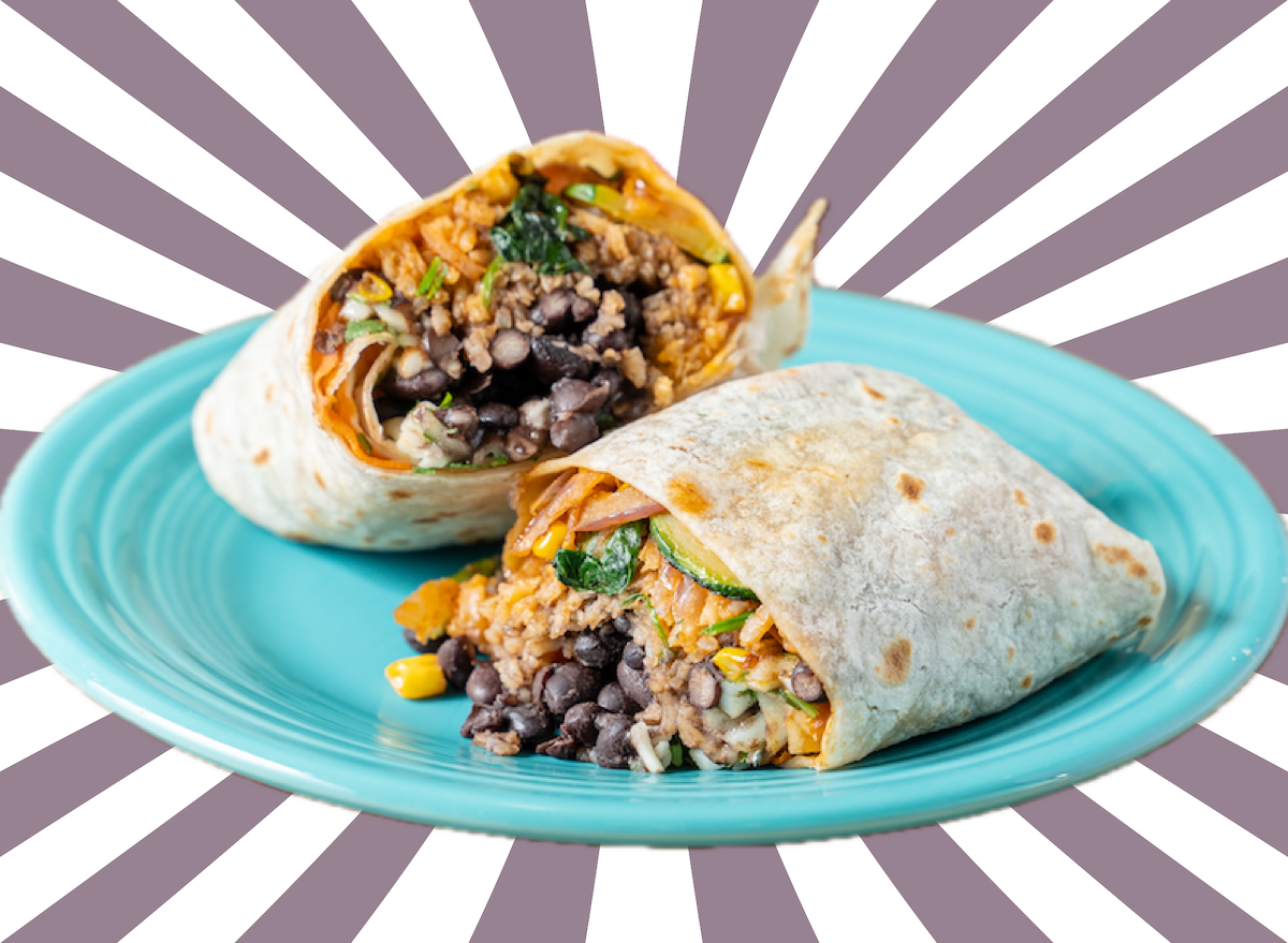 Burrito saudável cortado ao meio sobre uma mesa de madeira, ao lado de um notebook e uma garrafa de água