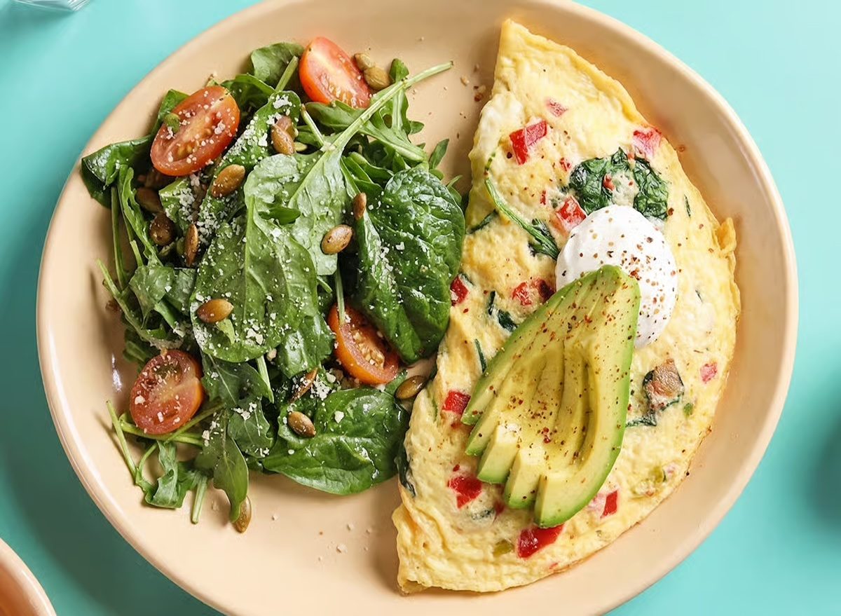Uma mulher preparando um omelete com vegetais e frutas frescas em uma frigideira de ferro