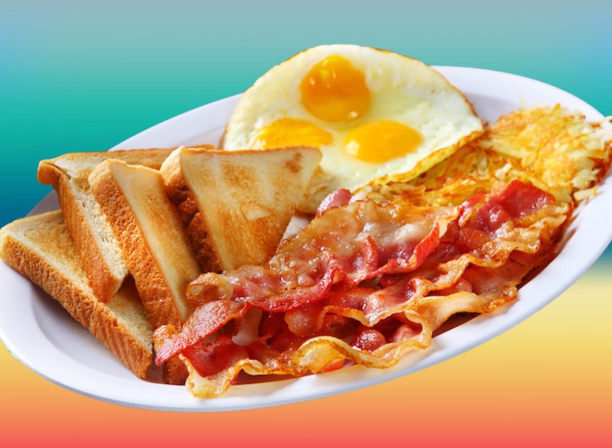 Prato com ovos mexidos, fatias de bacon, torrada integral, rodelas de abacate, morangos e castanhas espalhadas