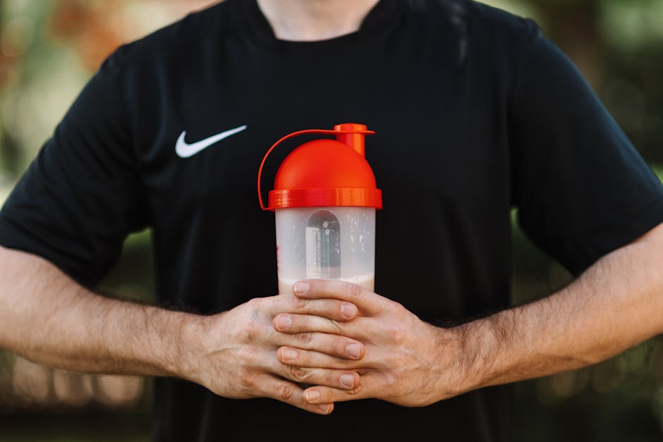 Atleta focado segurando uma coqueteleira ao lado de cápsulas de cafeína e um cronômetro sobre uma mesa de academia