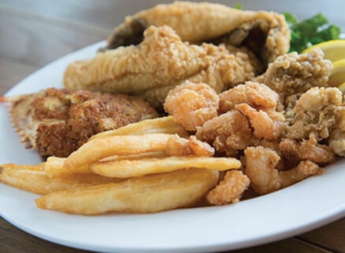 Filé de peixe empanado levemente com farinha de milho, dourado na frigideira, ao lado de limão e folhas de salsa