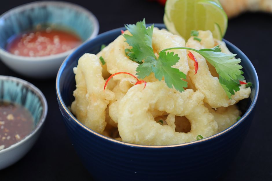 Um prato de calamari frito crocante sobre uma toalha de mesa branca, com um copo de água ao lado e um garfo à esquerda