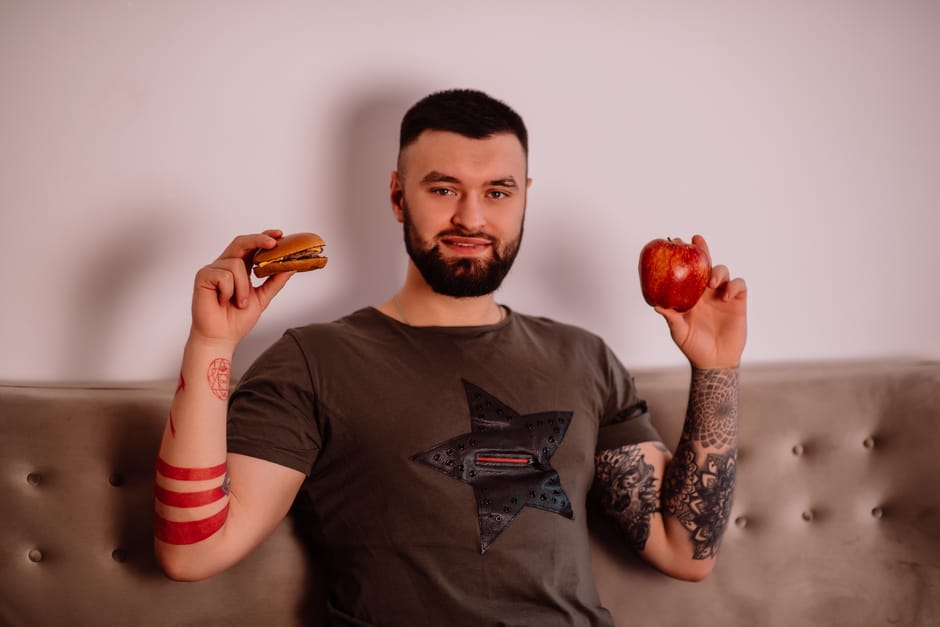 Mesa posta com sanduíche de fast-food, café e suco ao lado de uma balança de cozinha indicando alta densidade calórica
