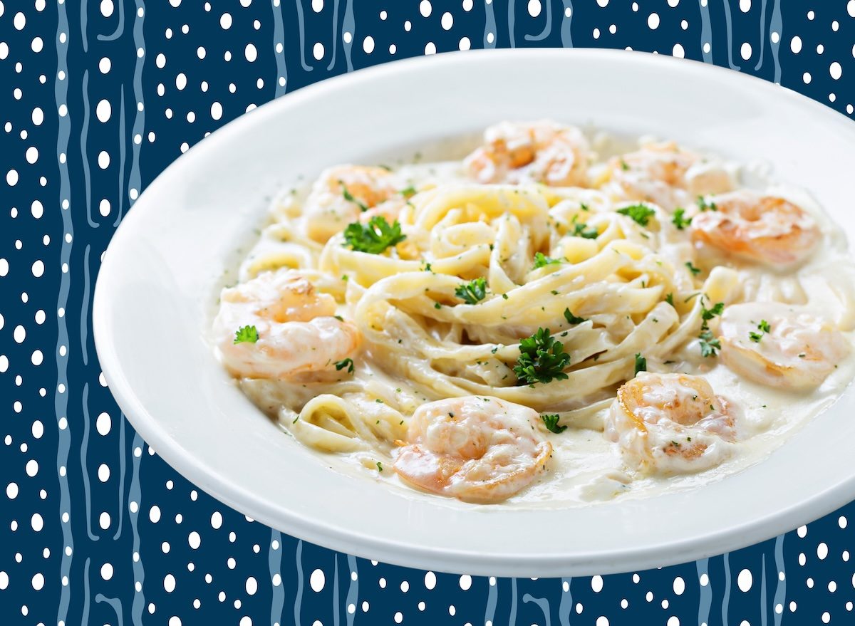 Prato de camarão ao alfredo com brócolis ao vapor, garfo e copo d'água sobre mesa de cozinha clara