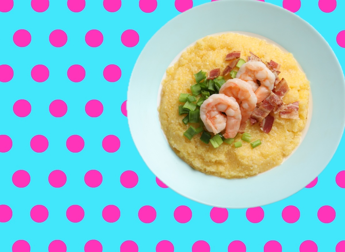 Prato de camarões grelhados sobre polenta cremosa, decorado com salsinha fresca e um garfo ao lado sobre a mesa
