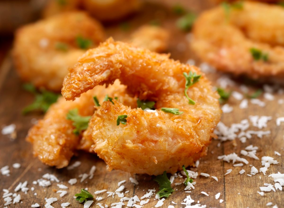 Camarões fritos dourados ao lado de batatas carregadas com queijo, bacon e cebolinha, sobre tábua de madeira