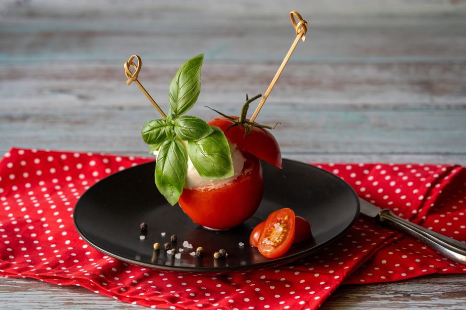Espetinhos coloridos com tomate‑cereja, mussarela de búfala, folhas de manjericão e fio de azeite sobre tábua