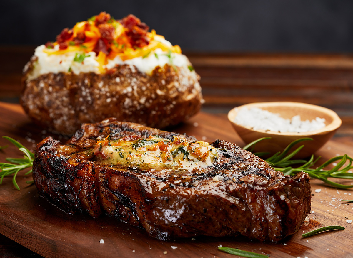 Bife de carne bovina grelhado ao lado de vegetais frescos em uma tábua de madeira, destacando a textura da proteína