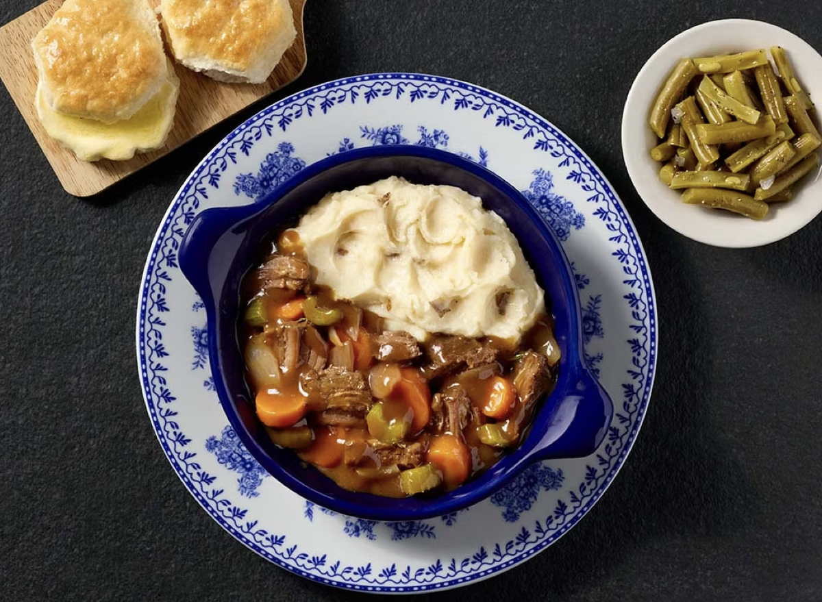 Carne de panela suculenta servida em prato cerâmico com legumes frescos e ervas sobre uma mesa de madeira rústica