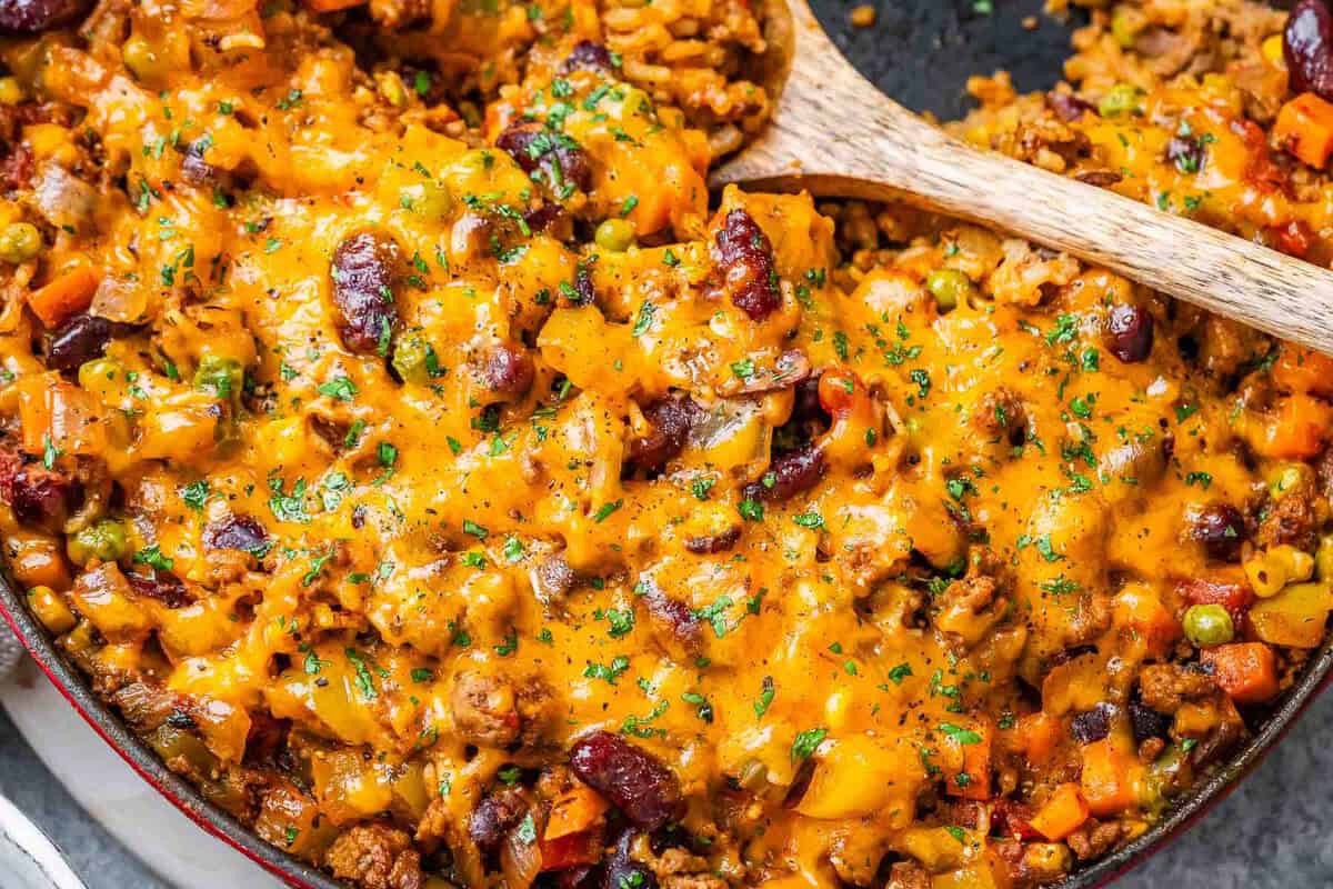 Panela de ferro com carne moída dourada, arroz soltinho e brócolis, cenoura e pimentão coloridos, ao lado de garrafa d'água