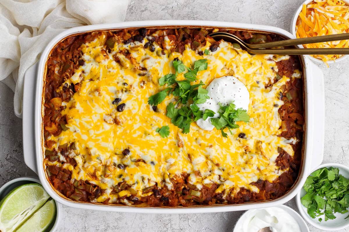 Travessa de cerâmica com enchilada de frango dourada, decorada com coentro fresco e fatias de abacate ao lado