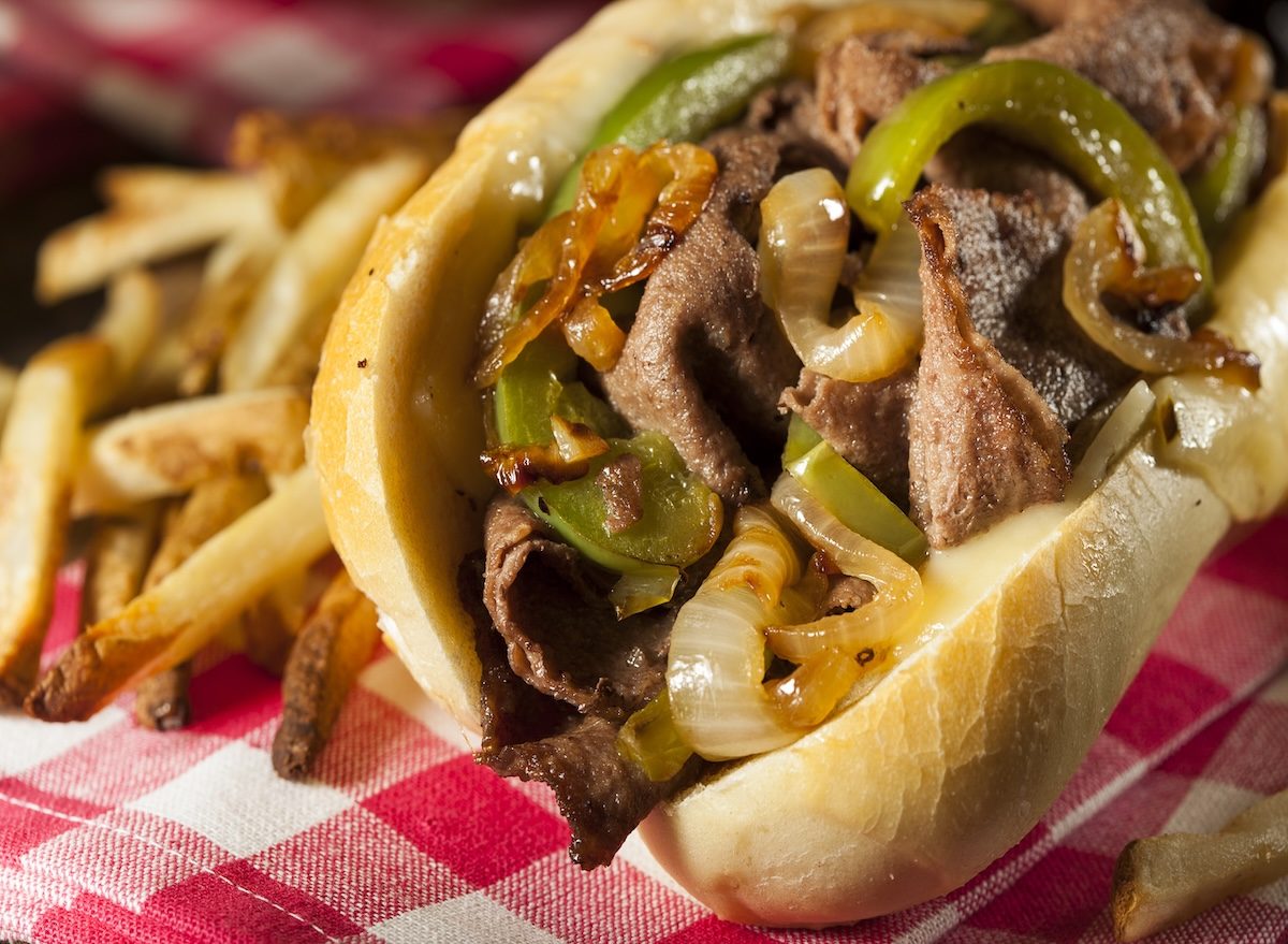 Tiras de carne grelhada, queijo derretido escorrendo e pão macio ao lado de batatas assadas e folhas de rúcula