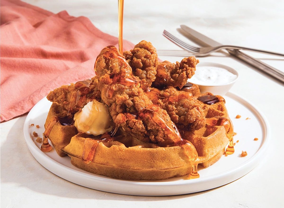 Frango frito crocante ao lado de waffles dourados, cobertos com mel e acompanhados de folhas de rúcula