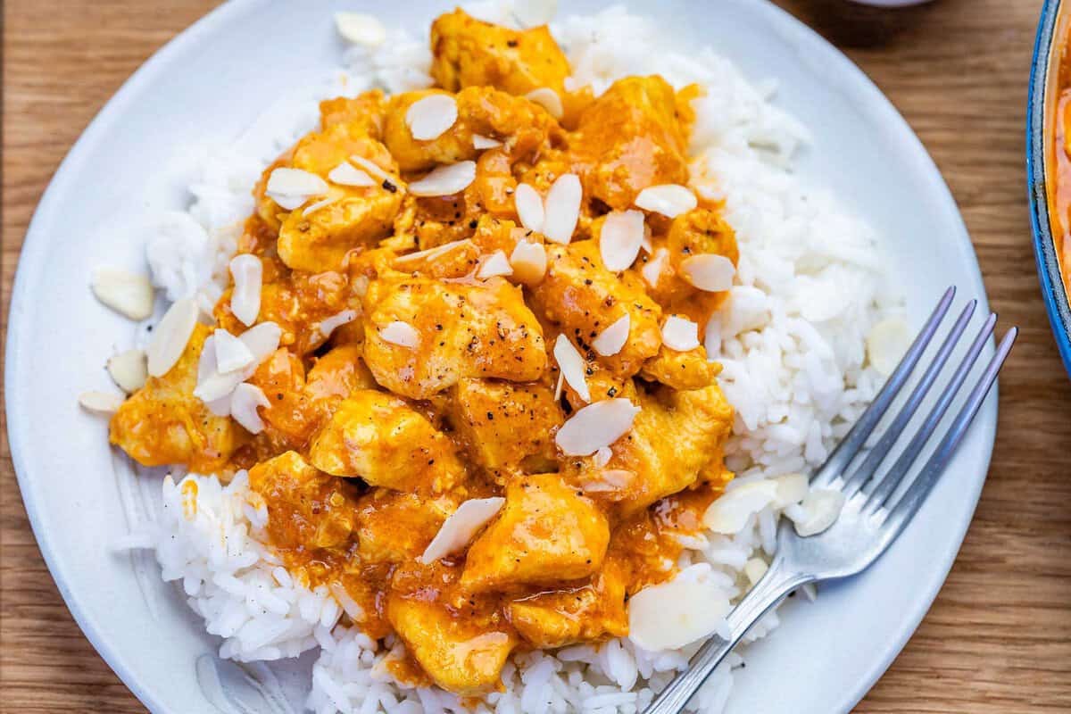 Peito de frango dourado em molho korma cremoso ao lado de iogurte grego, arroz integral e coentro fresco