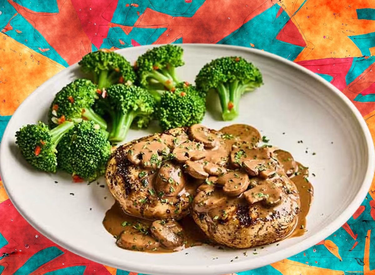 Prato de Chicken Marsala ao lado de salada verde, frigideira com cogumelos e taça de água, em bancada de cozinha clara