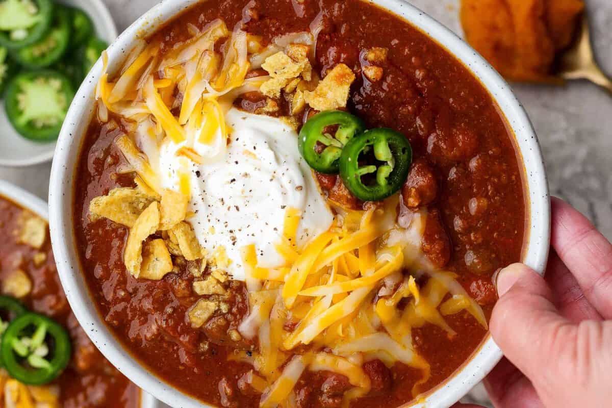 Panela de slow cooker aberta mostrando chili de abóbora com cubos de carne, feijão vermelho e folhas de coentro