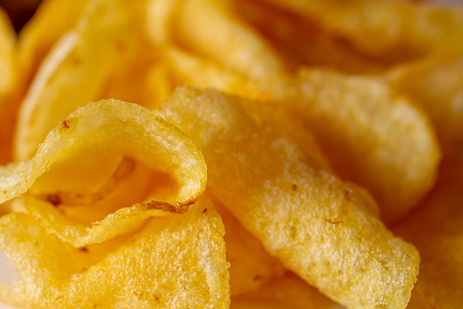 Mãos segurando chips dourados ao lado de uma tigela de salsa verde com limão e coentro
