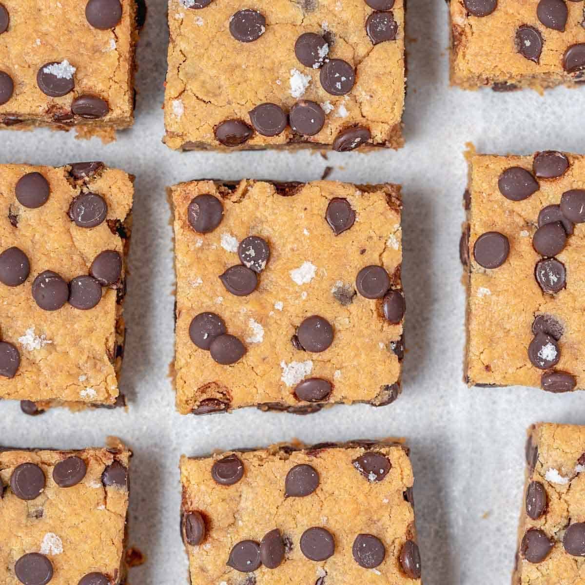 Pedaços de chocolate e barras de proteína em uma tábua de cozinha, rodeadas por utensílios de cozinha e ingredientes variados