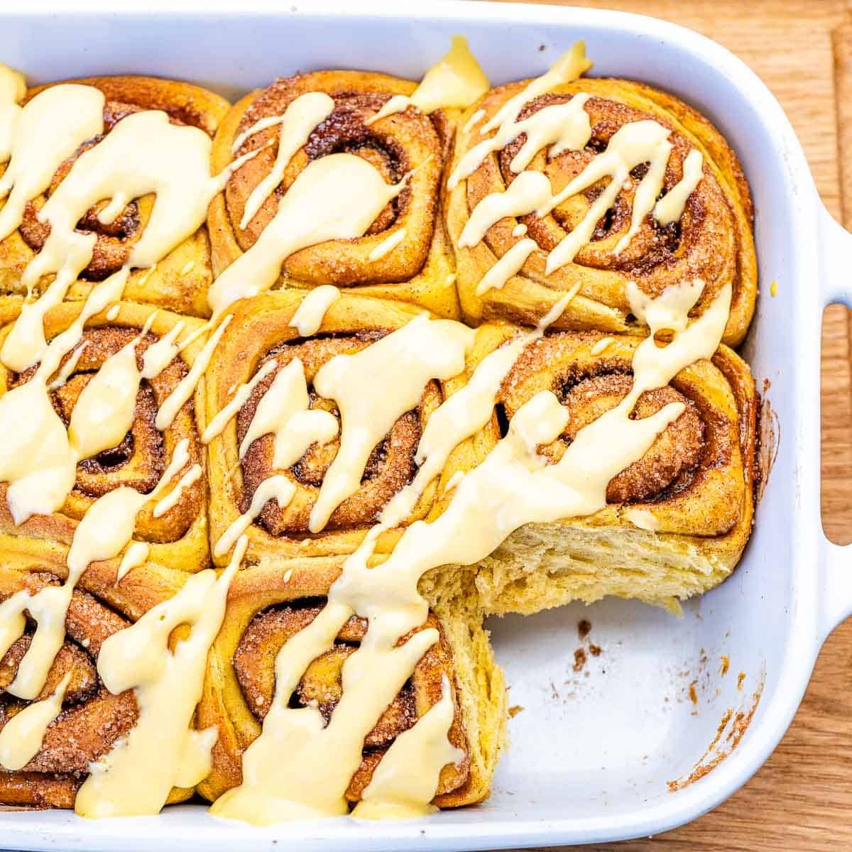 Rolinhos de abóbora com canela sobre prato branco, cobertos por glaze de iogurte grego e cream cheese, ao lado de frutas vermelhas