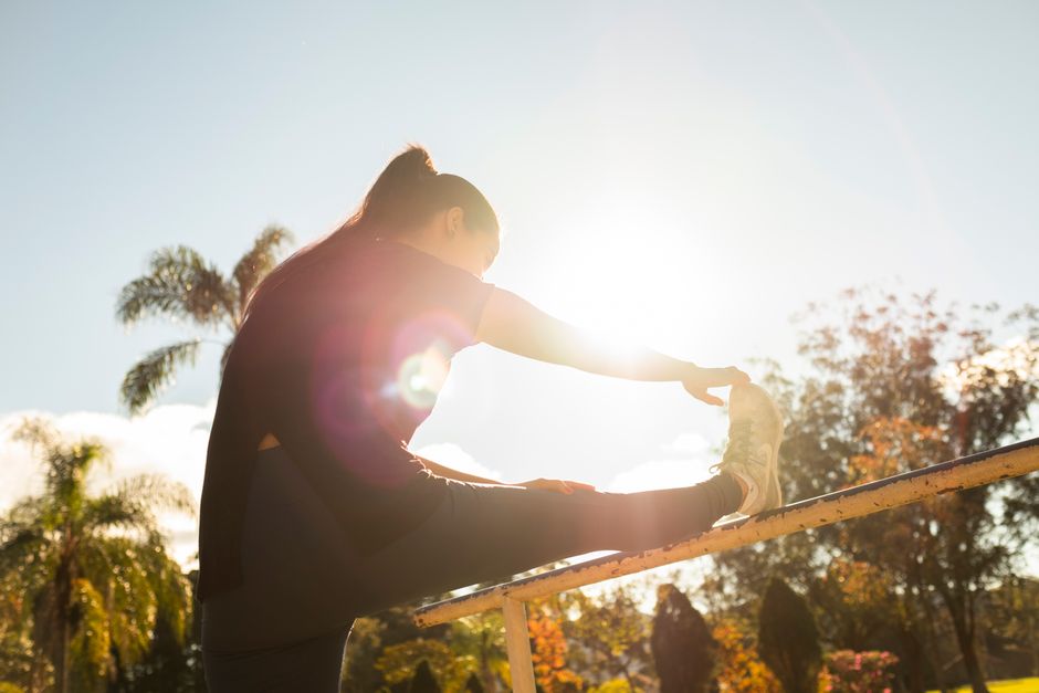 Mulher em pijama de treino, fazendo prancha lateral ao lado de um copo de água com rodelas de limão e um tapete de yoga