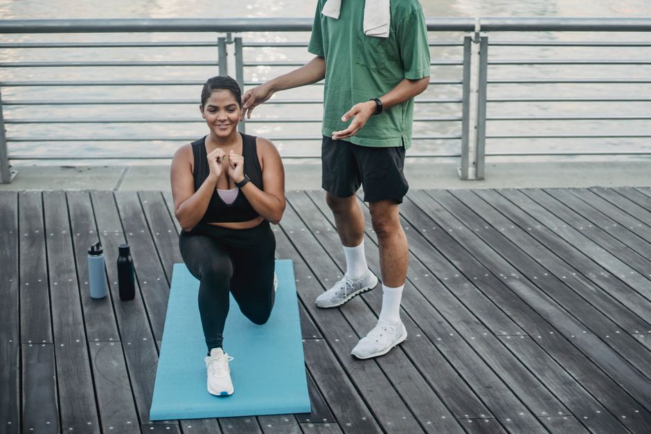 Um personal trainer orienta um cliente em frente a um quadro de metas, segurando um haltere e anotando progresso num tablet